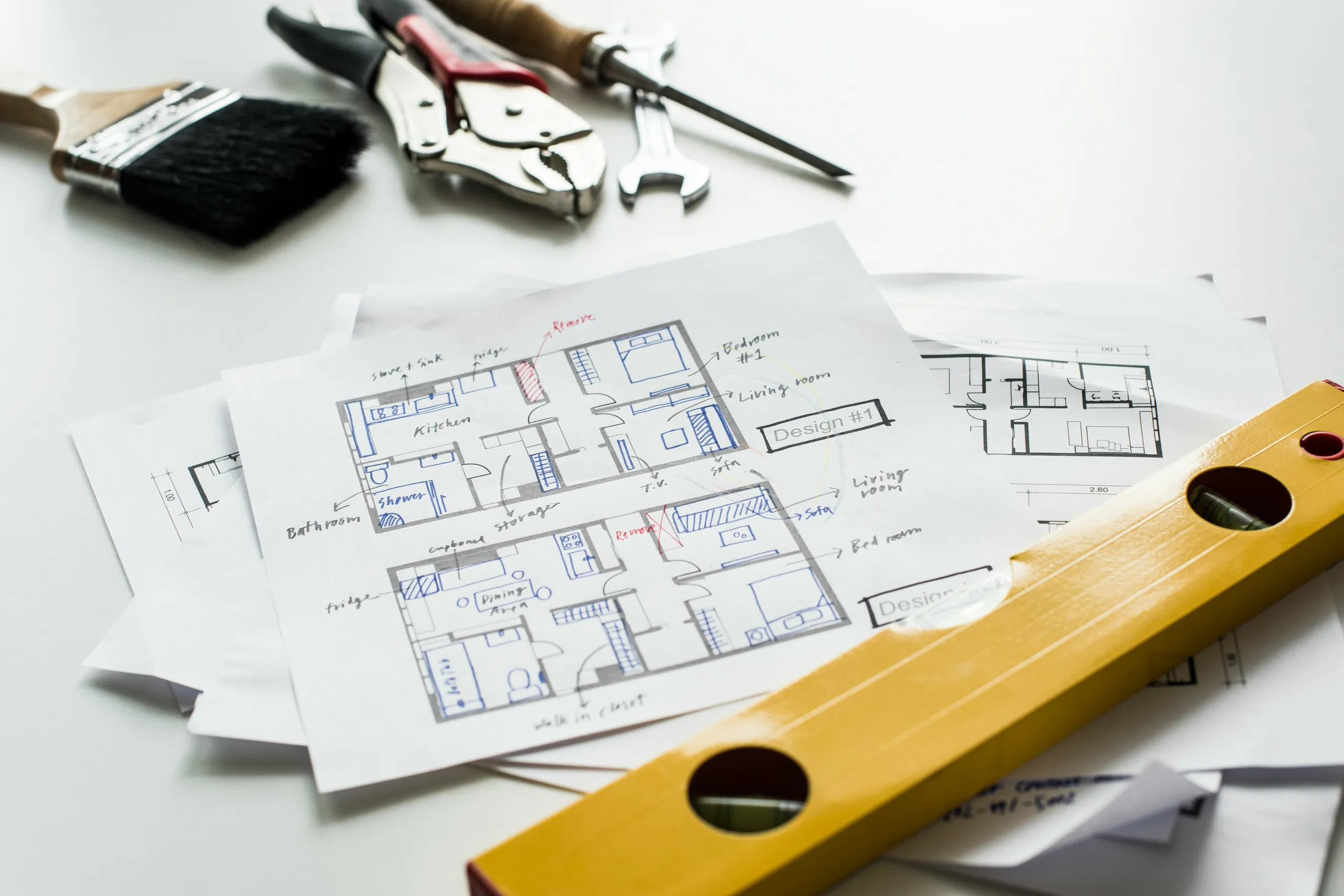 Planos técnicos de una vivienda con anotaciones a mano, junto a un nivel y herramientas