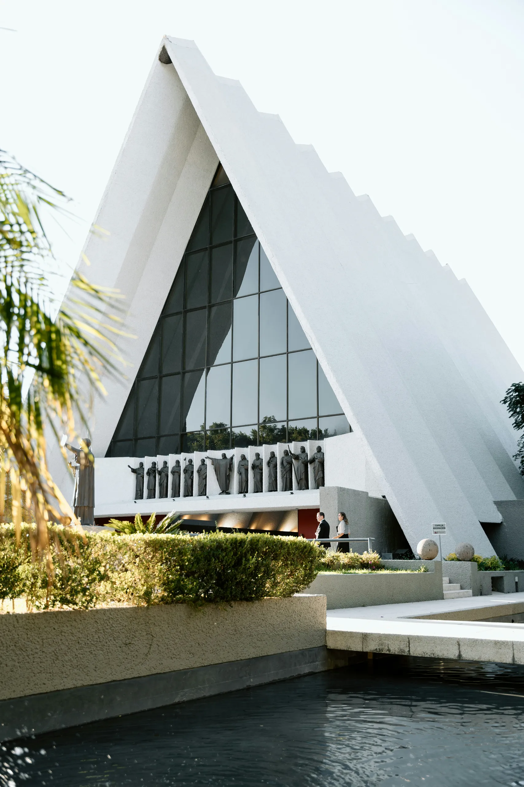 Capilla de hormigón de volumen triangular, tipo carpa, con gran acristalamiento y una fila de esculturas sobre la entrada